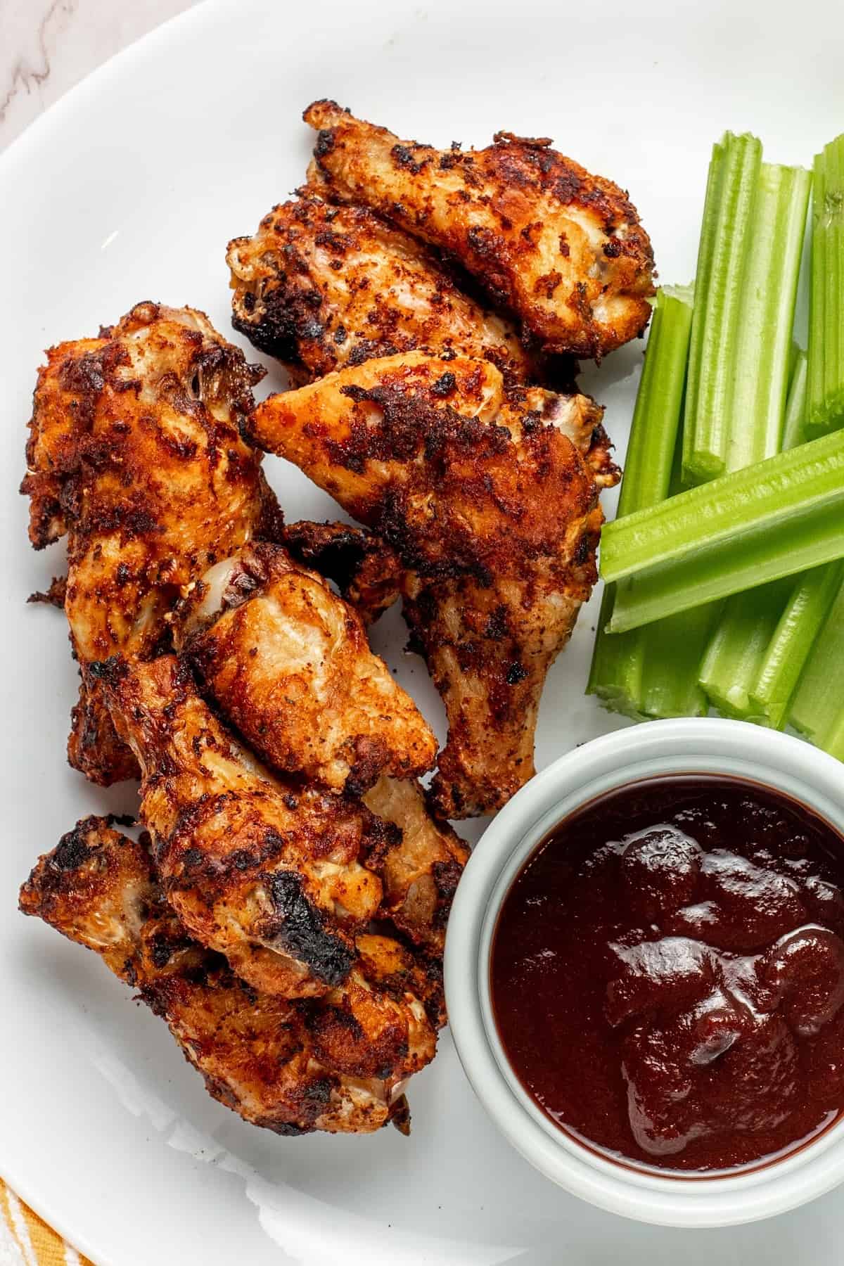 air fryer frozen chicken wings on a plate with celery sticks and a small bowl of barbecue sauce