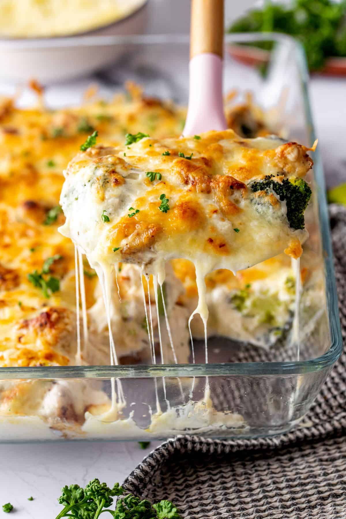 A photo of a person lifting a scoop of Chicken Alfredo Casserole from a casserole dish