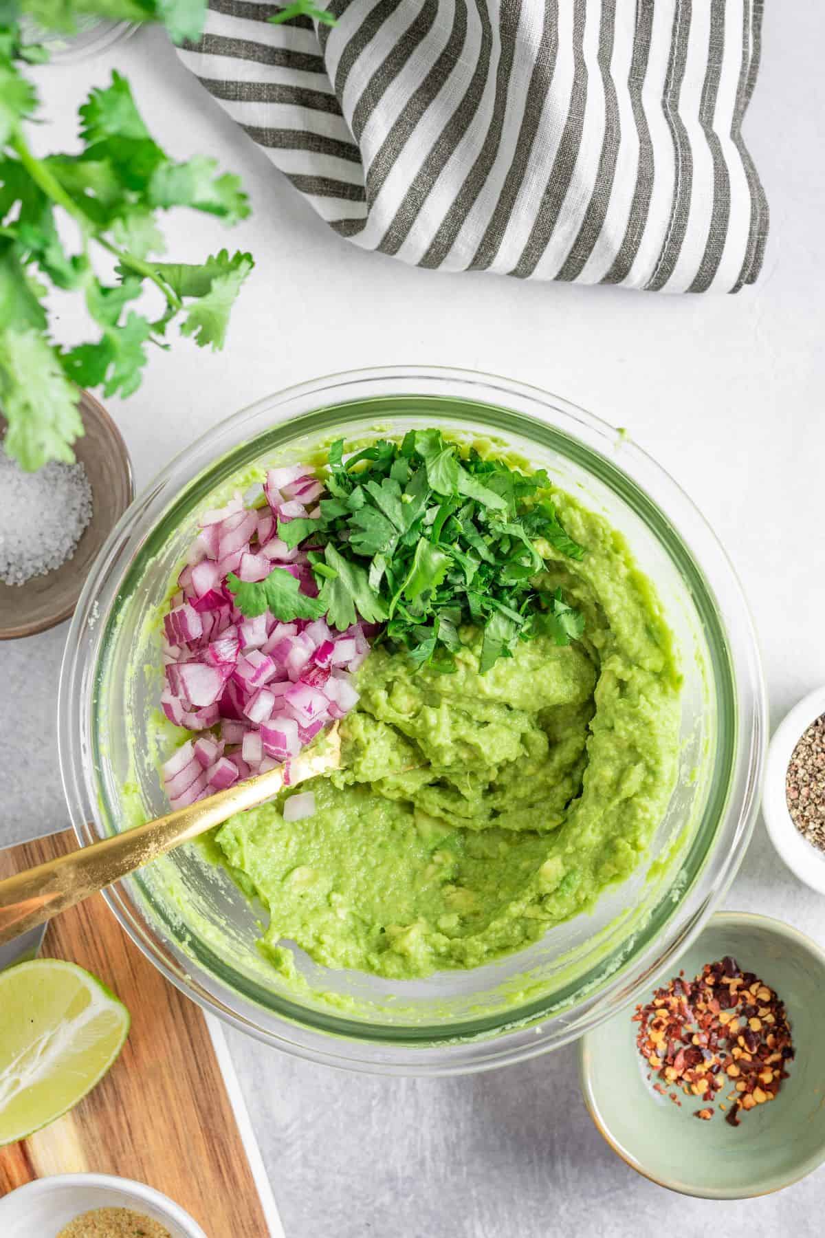 mixing avocado, onions, cilantro and spices on a large bowl