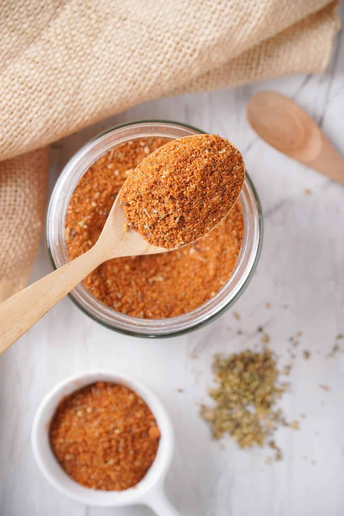 spoonful of homemade bbq seasoning next to a jar of bbq dry rub