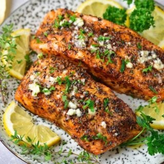 two air fryer salmon filets on a plate topped with garlic butter