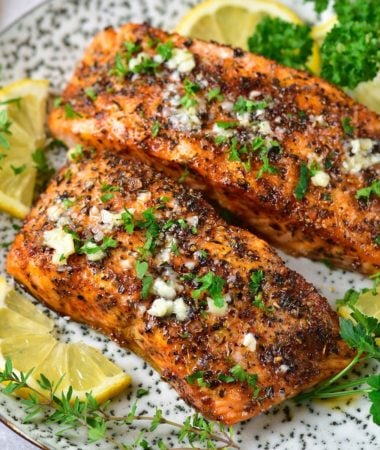 two air fryer salmon filets on a plate topped with garlic butter