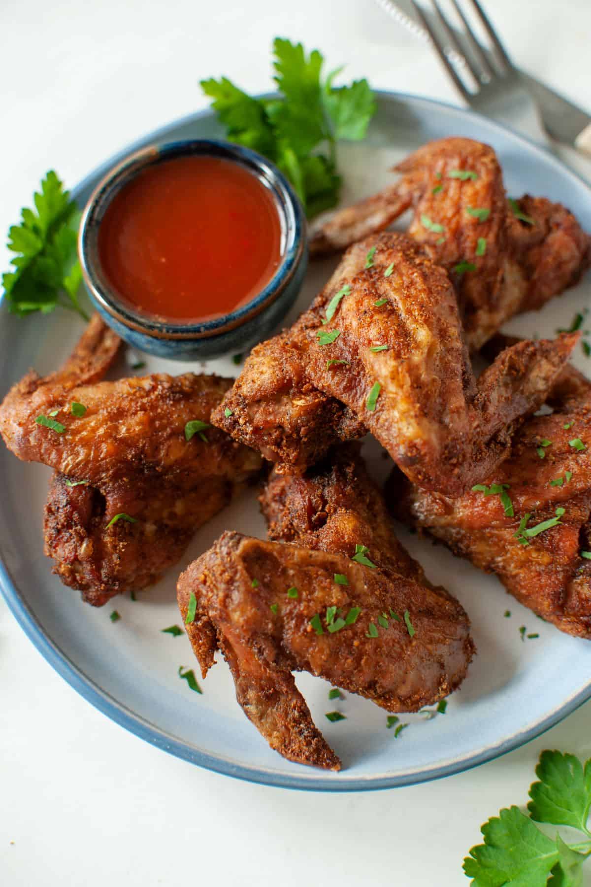 Overhead view of a plate of wings, garnished with parsley, with a bowl of dipping sauce