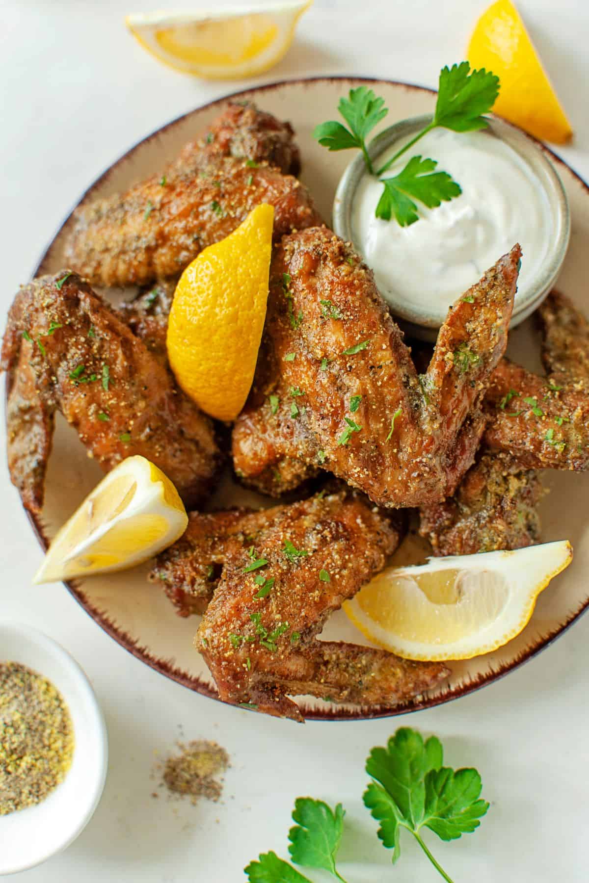 crispy air fryer Lemon Pepper Wings on a plate with lemon slices and ranch dressing as a dip