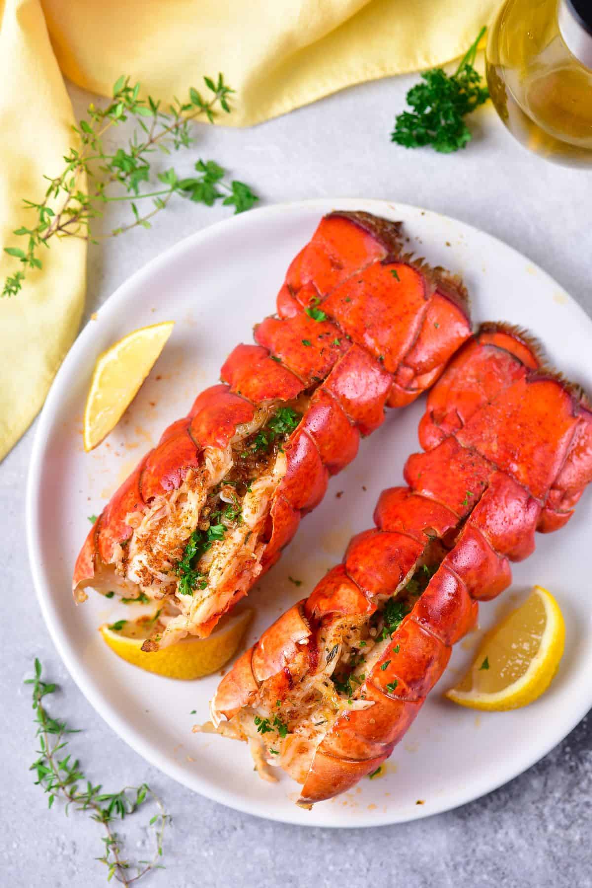 Two air fryer Lobster Tails on a plate topped with garlic butter, parsley and lemon slices