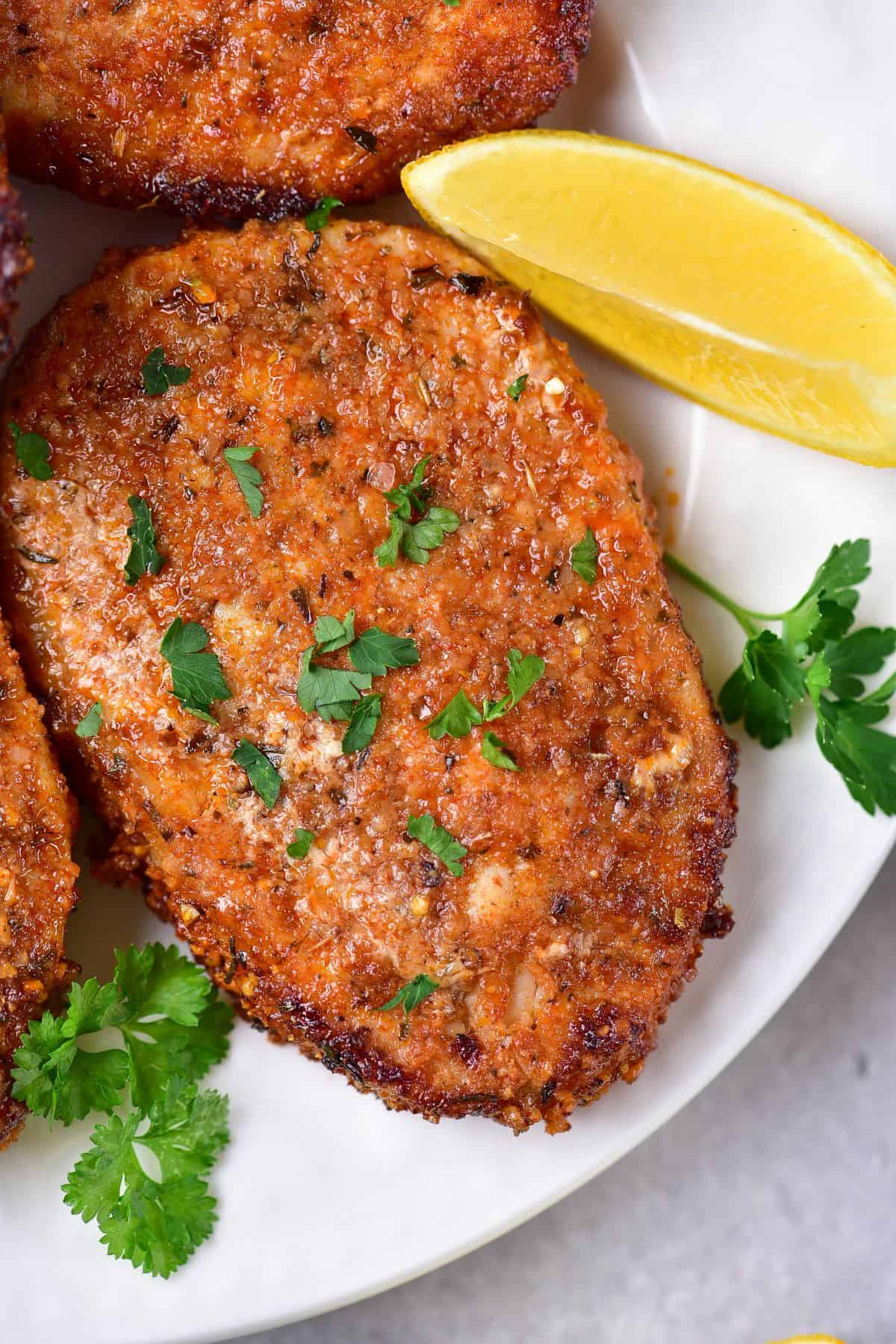 crispy air fryer Pork Chops on a plate with lemon slices and parsley