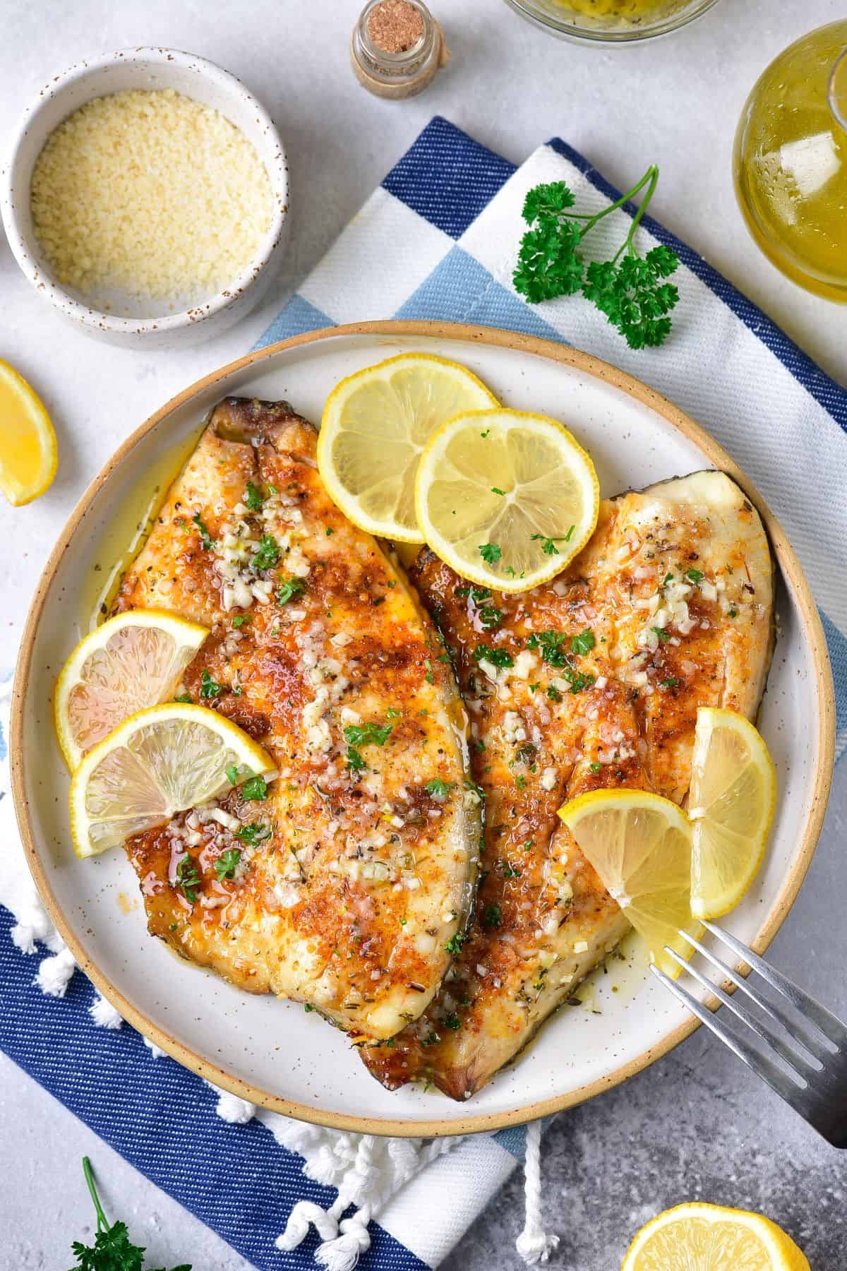 cooked air fryer Tilapia with lemon slices and garlic butter on a plate