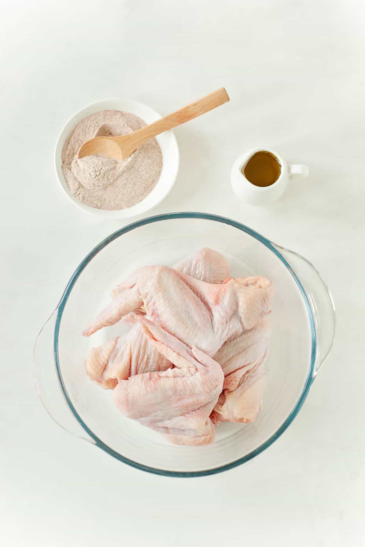 chicken wings on a large bowl, olive oil and mixed spices on a small bowl