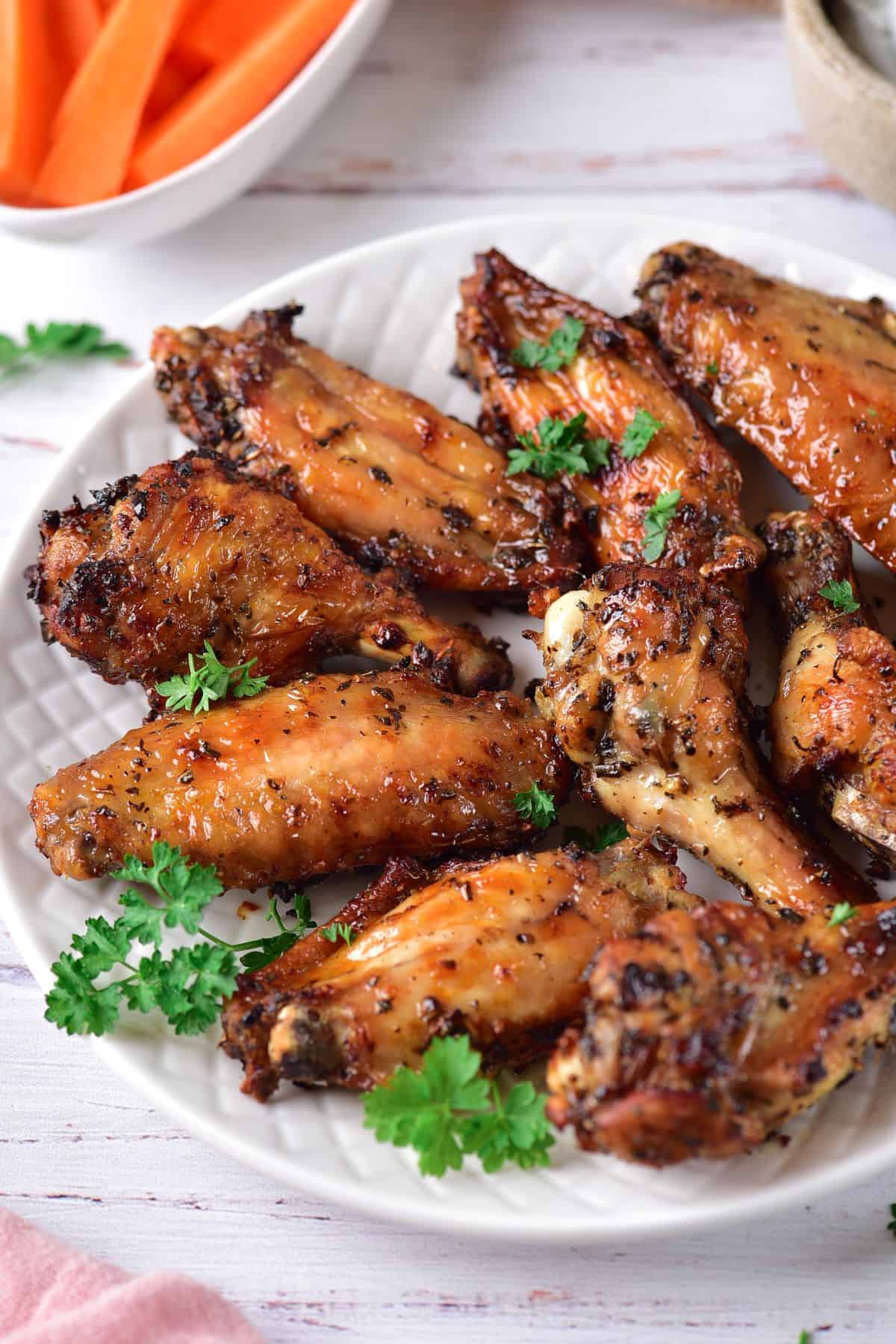 Marinated good Chicken Wings on a large plate with fresh parsley and carrot sticks