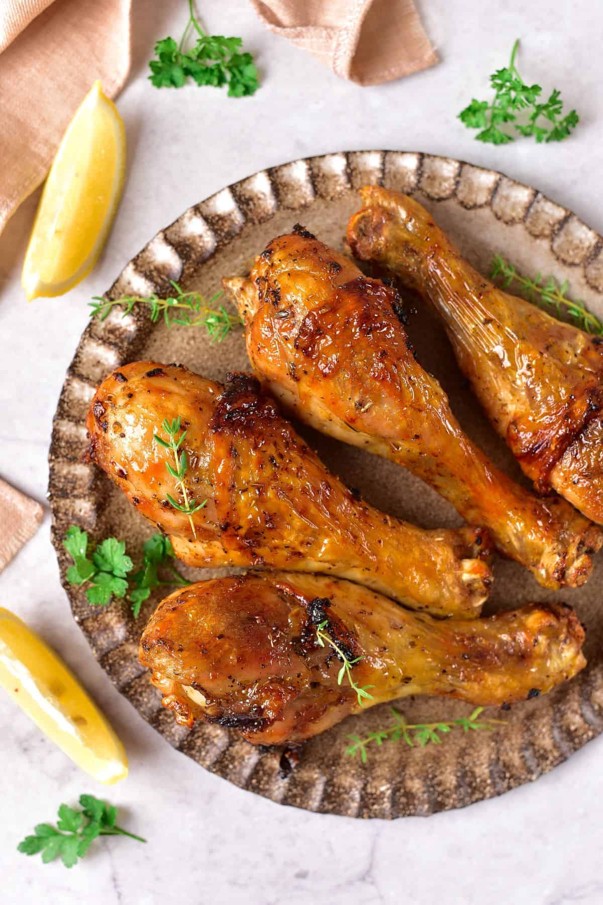 cooked Marinated chicken Drumsticks on a plate surrounded with slices of lemon and fresh herbs
