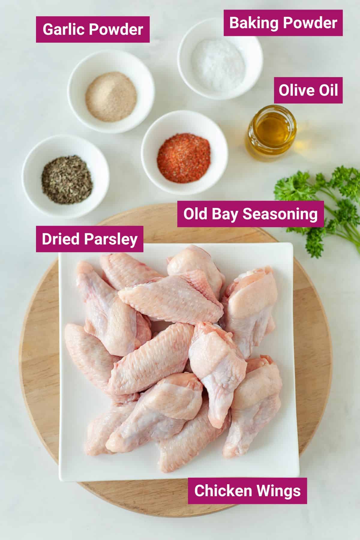 baking powder, olive oil, old bay seasoning, dried parsley, and chicken wings on separate bowls