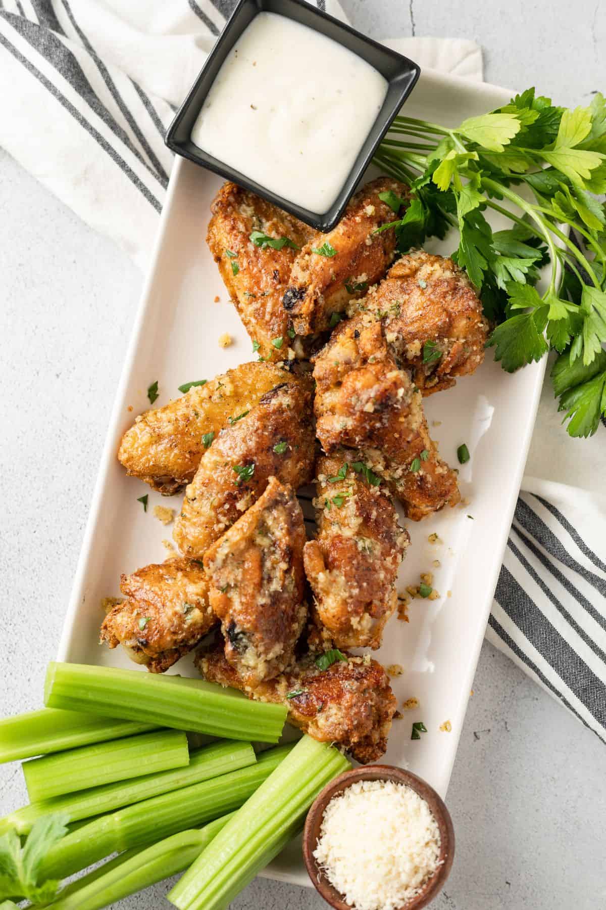 Baked Garlic Parmesan Wings on a rectangular plate with celery sticks, parsley, and parmesan cheese