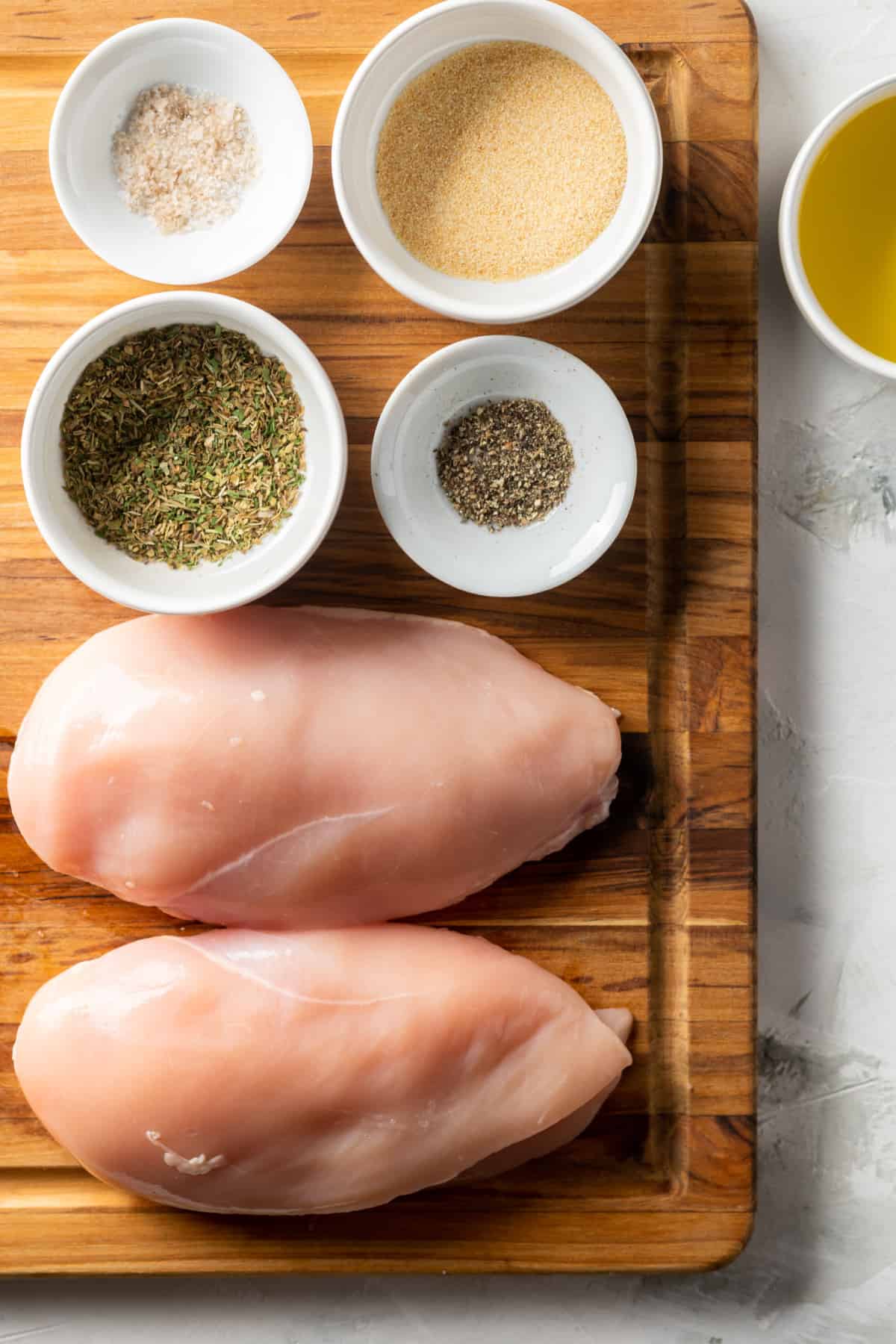 a photo of the ingredients for cast iron chicken breasts, including olive oil, garlic powder, black pepper, salt and Italian seasoning.