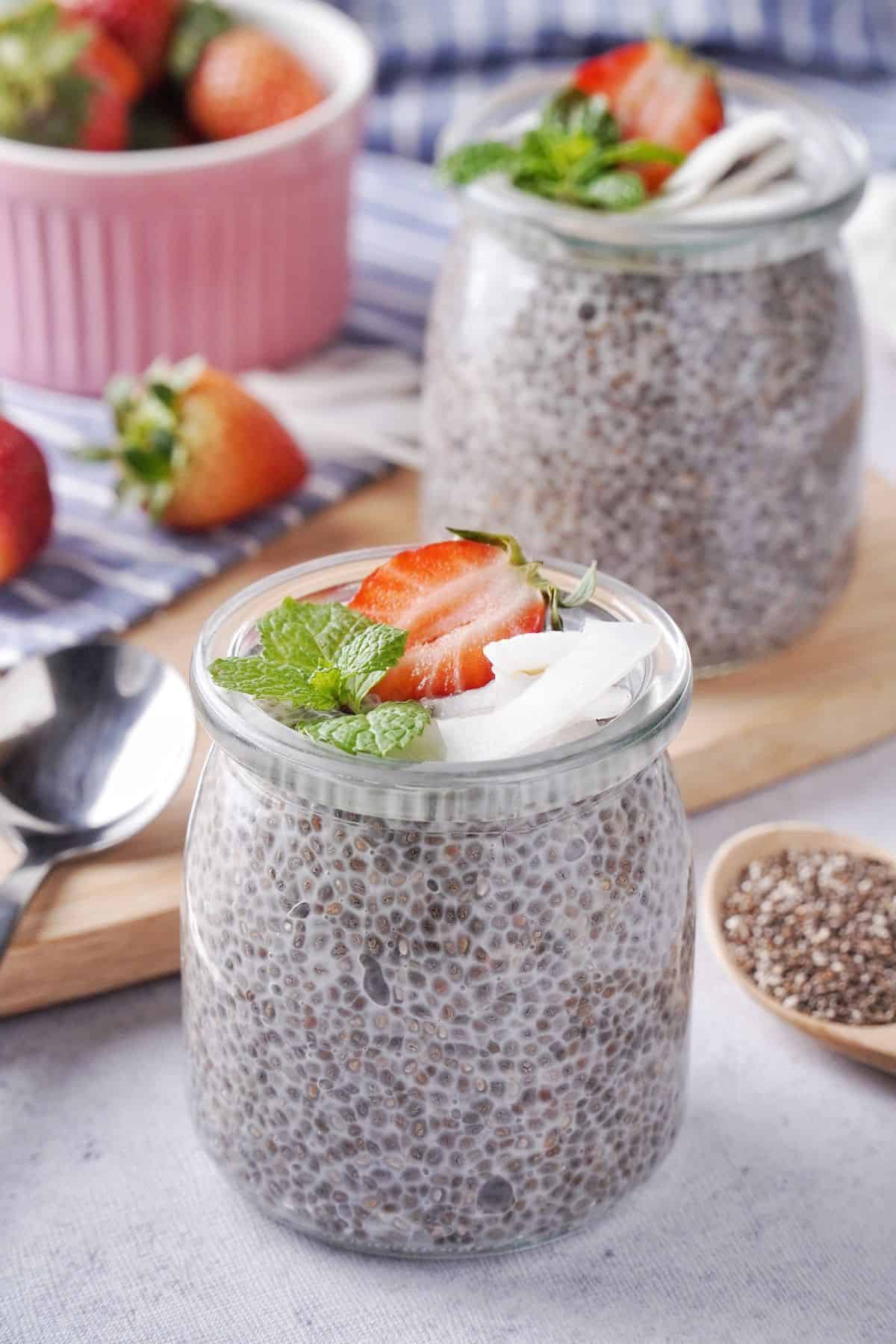 Chia Seed Pudding With Coconut Milk in a clear mug topped with sliced strawberries and coconut slices