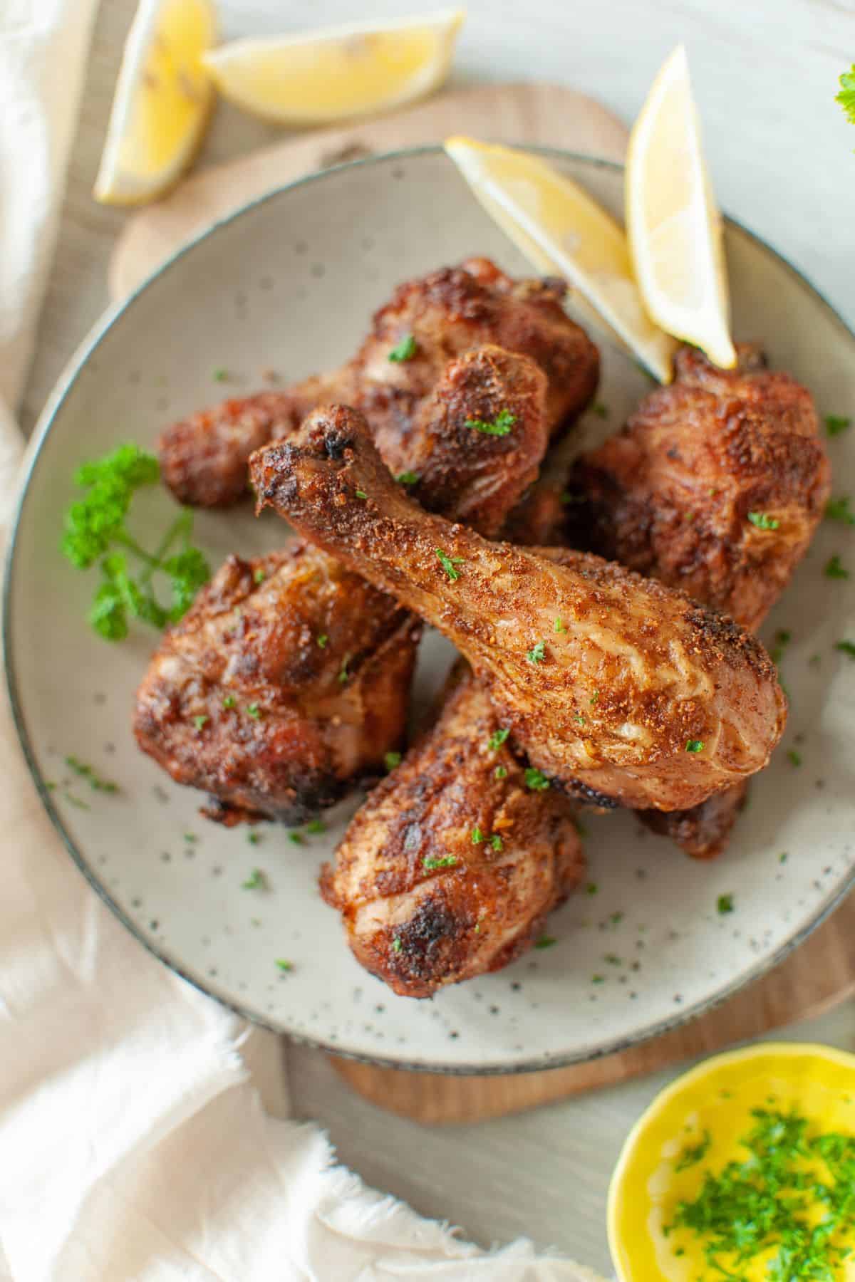 Overhead view of chicken drumsticks on a plate, garnished with parsley, with 2 lemon slices