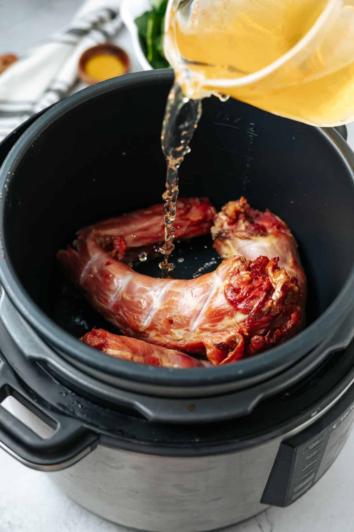 pouring chicken broth to the Smoked turkey necks on o a cooker pot