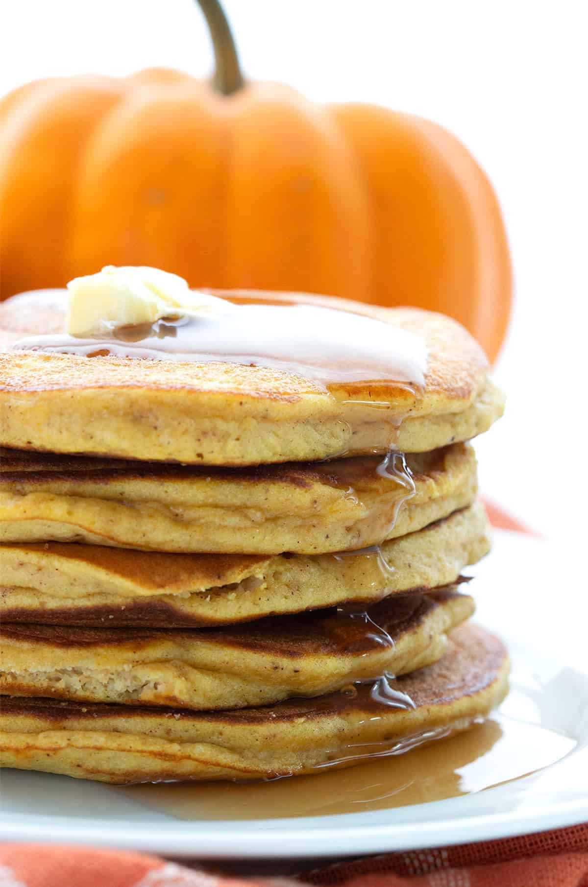 a stack of keto pumpkin pancakes on a plate with a fresh pumpkin behind them