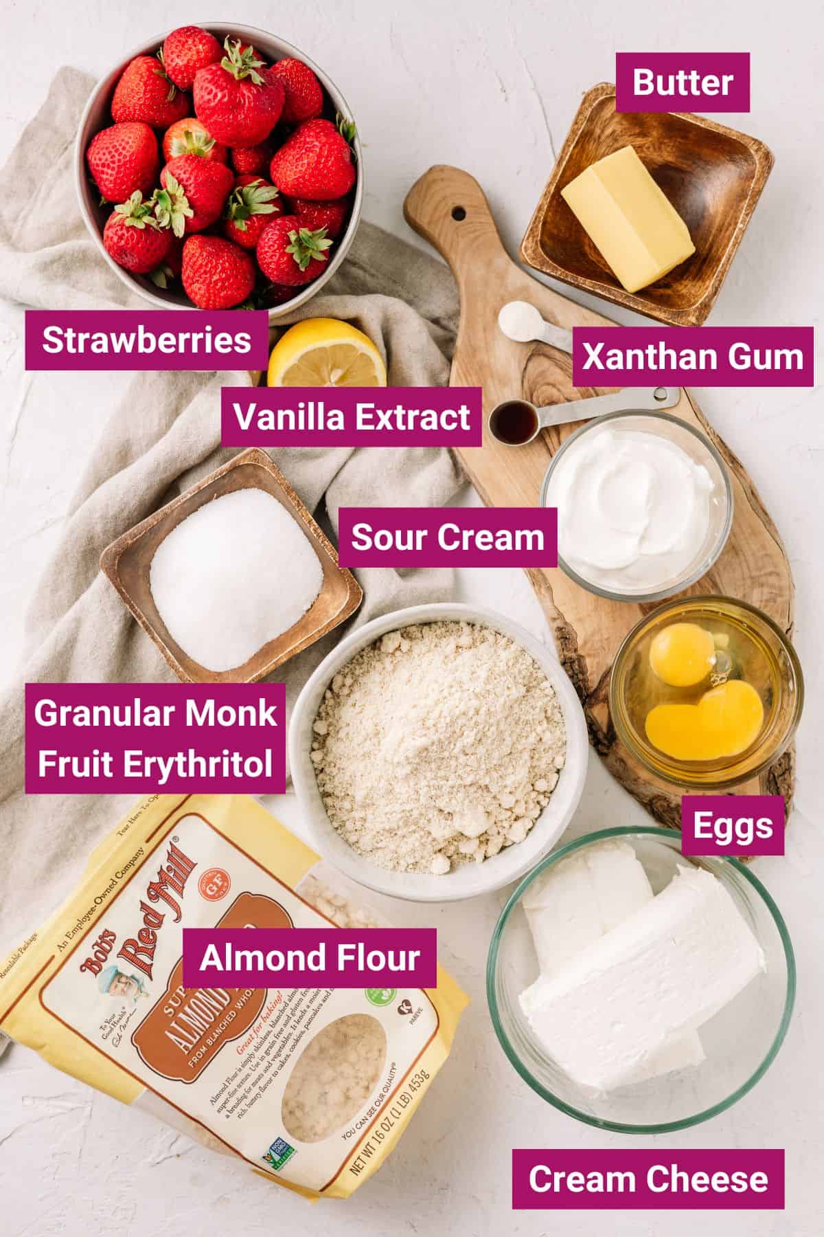 butter, strawberries, vanilla extract, sour cream, xanthan gum, eggs, granular mnk fruit erythritol, eggs, almond flour and cream cheese on separate bowls