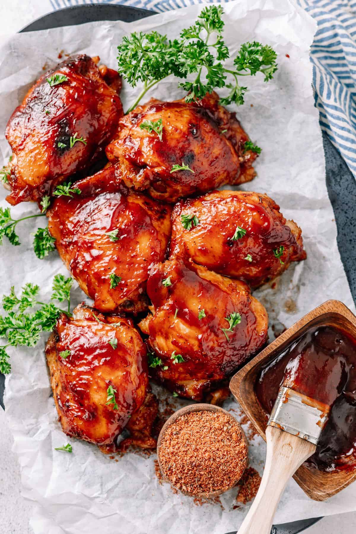 juicy slow cooker Crockpot BBQ Chicken Thighs on plate with parchment paper and bbq seasoning