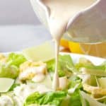 pouring Creamy Caesar Salad Dressing to the chicken and lettuce