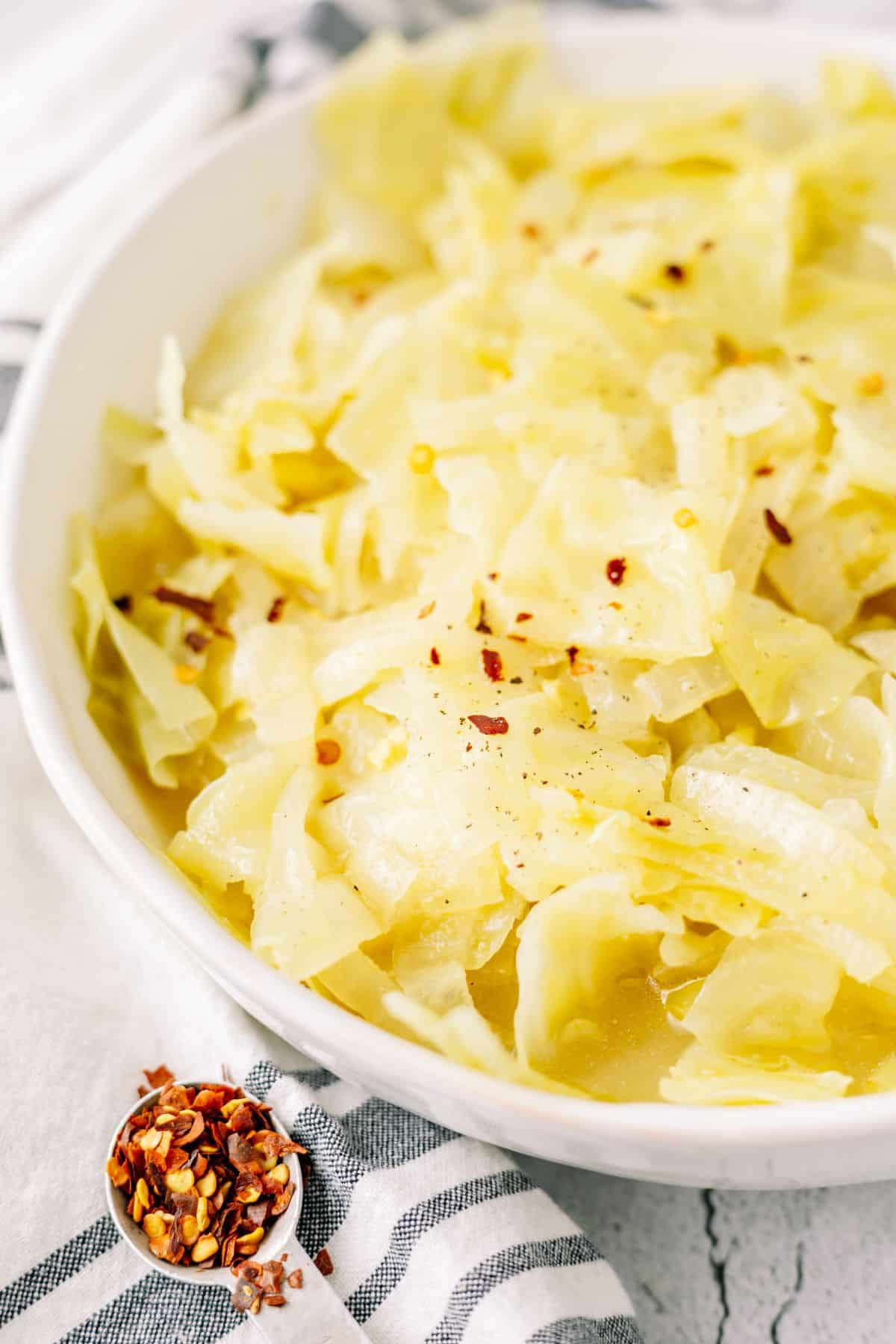 cooked cabbage topped with red pepper flakes on a large white bowl