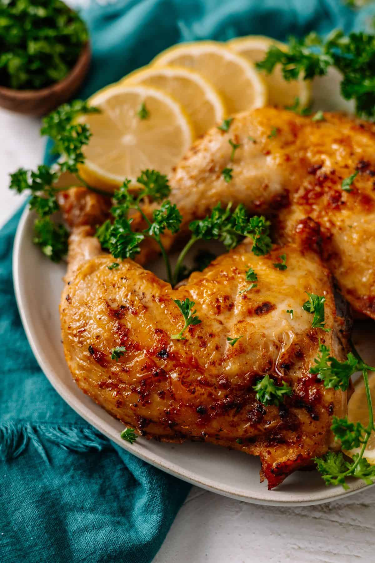 Juicy air fryer chicken leg quarters next to lemon slices on a plate.