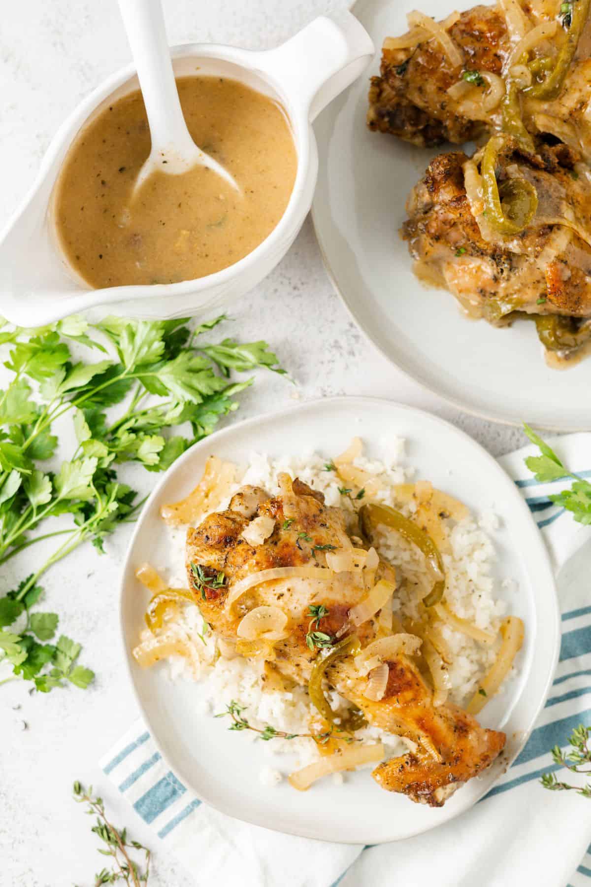 Overhead view of a plate with a turkey wing on top of cauliflower rice, next to a boat of gravy, fresh parsley, and a plate with another wing