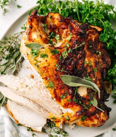 A turkey breast on a plate, cut into slices, covered in herbs