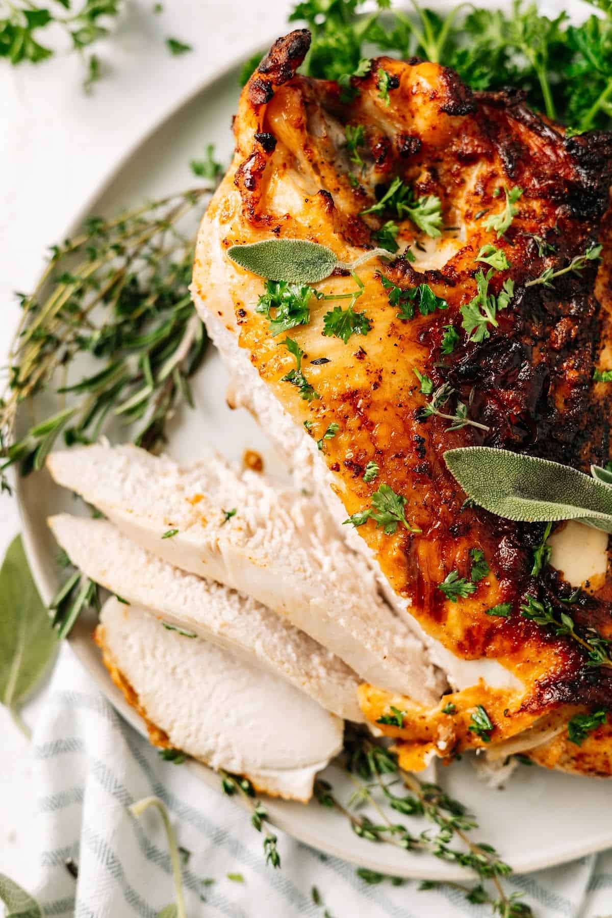 Close up overhead view of a plate with a turkey breast cut into slices, covered in herbs