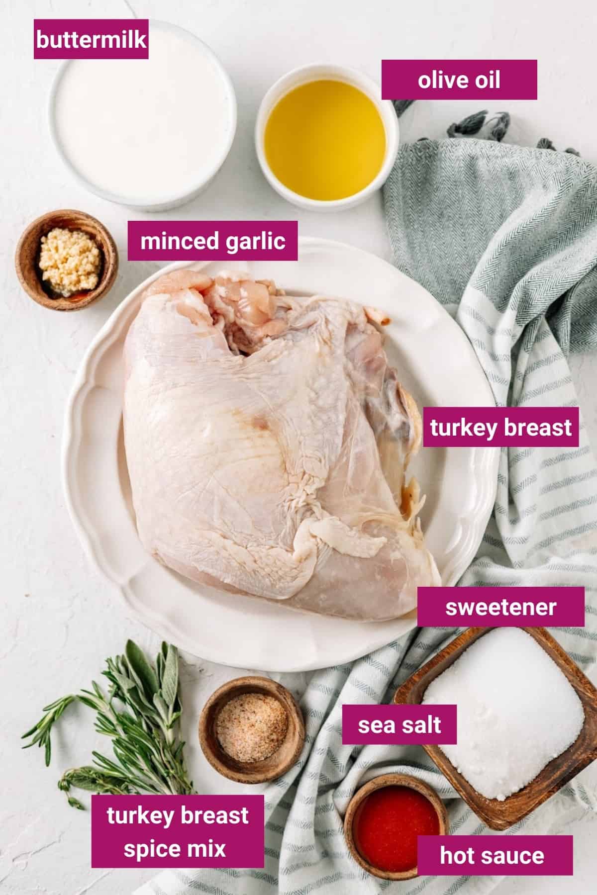 Overhead view of the labeled ingredients for air fryer turkey breasts: turkey breast, minced garlic, buttermilk, olive oil, sweetener, sea salt, hot sauce, and turkey breast spice mix