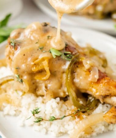 Close up of a turkey wing on top of cauliflower rice, on a plate, with a spoon pouring gravy over the top