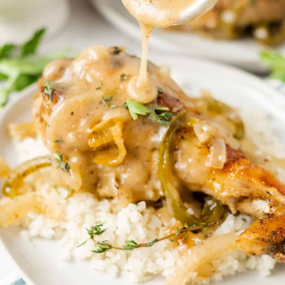 Close up of a turkey wing on top of cauliflower rice, on a plate, with a spoon pouring gravy over the top