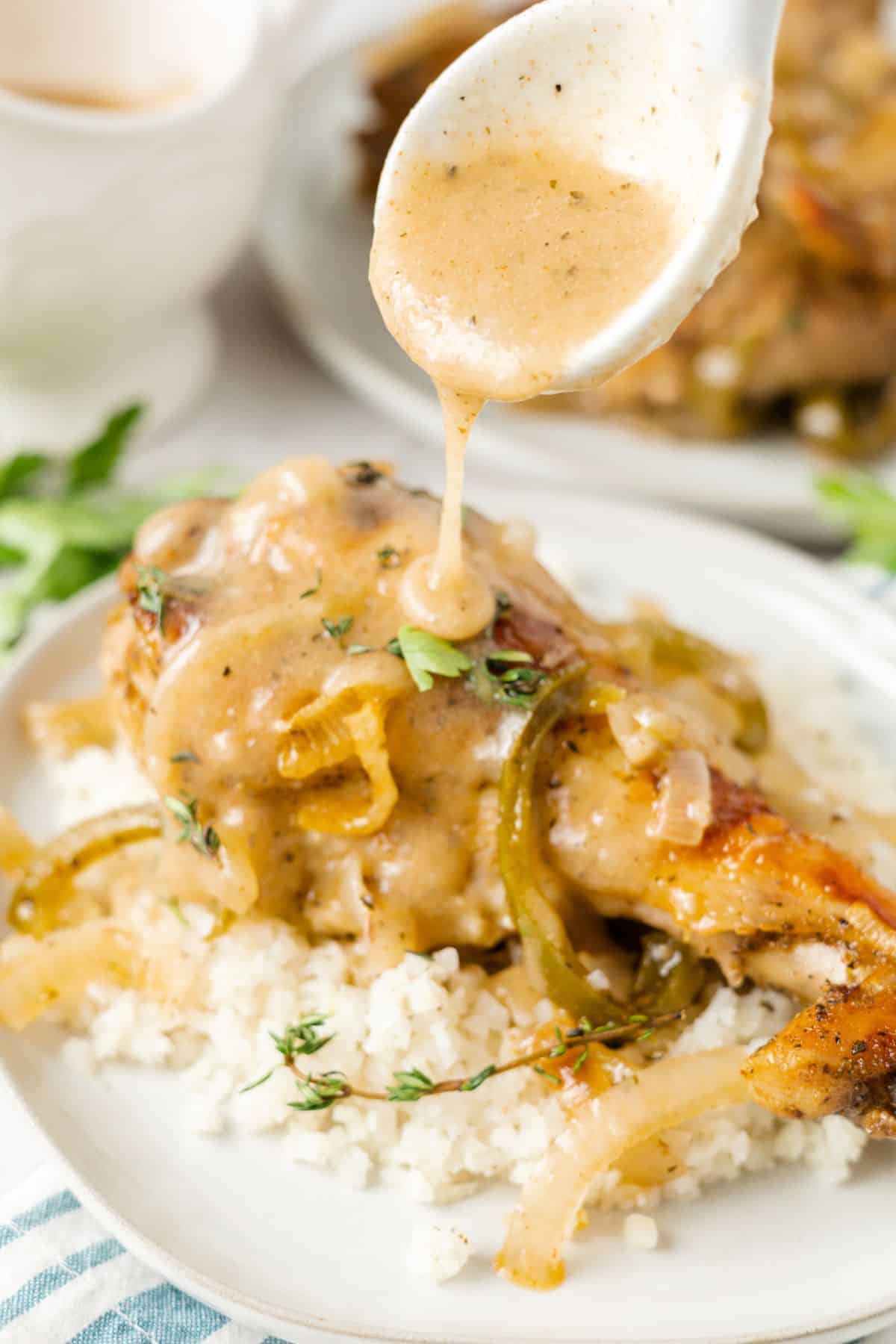 A spoon pouring graving over a turkey wing on top of cauliflower rice on a plate