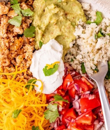 a photo of a healthy taco bowl with ground turkey, sour cream, guacamole, tomatoes, red onions, cheese, and cilantro lime cauliflower rice