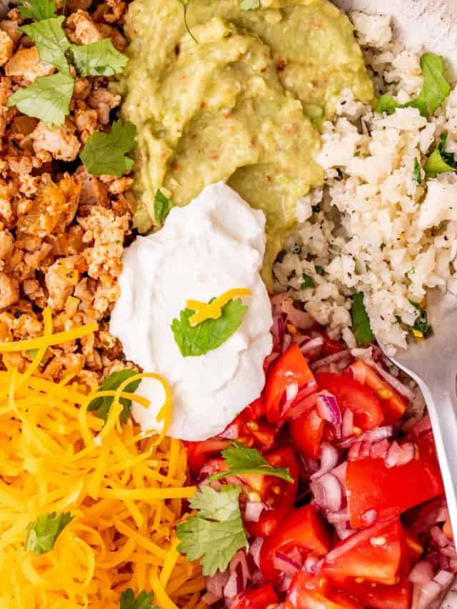 a photo of a healthy taco bowl with ground turkey, sour cream, guacamole, tomatoes, red onions, cheese, and cilantro lime cauliflower rice