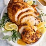 close-up photo of tender pressure cooker turkey breast on a plate with lemon slices, turkey gravy and fresh herbs