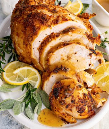 close-up photo of tender pressure cooker turkey breast on a plate with lemon slices, turkey gravy and fresh herbs