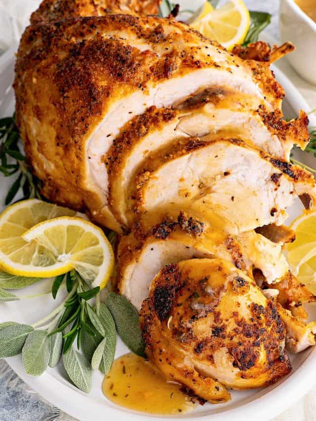 close-up photo of tender pressure cooker turkey breast on a plate with lemon slices, turkey gravy and fresh herbs