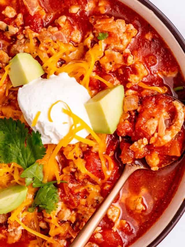 a close up of a bowl of keto taco soup with avocado, sour cream, cilantro, and shredded cheese on top