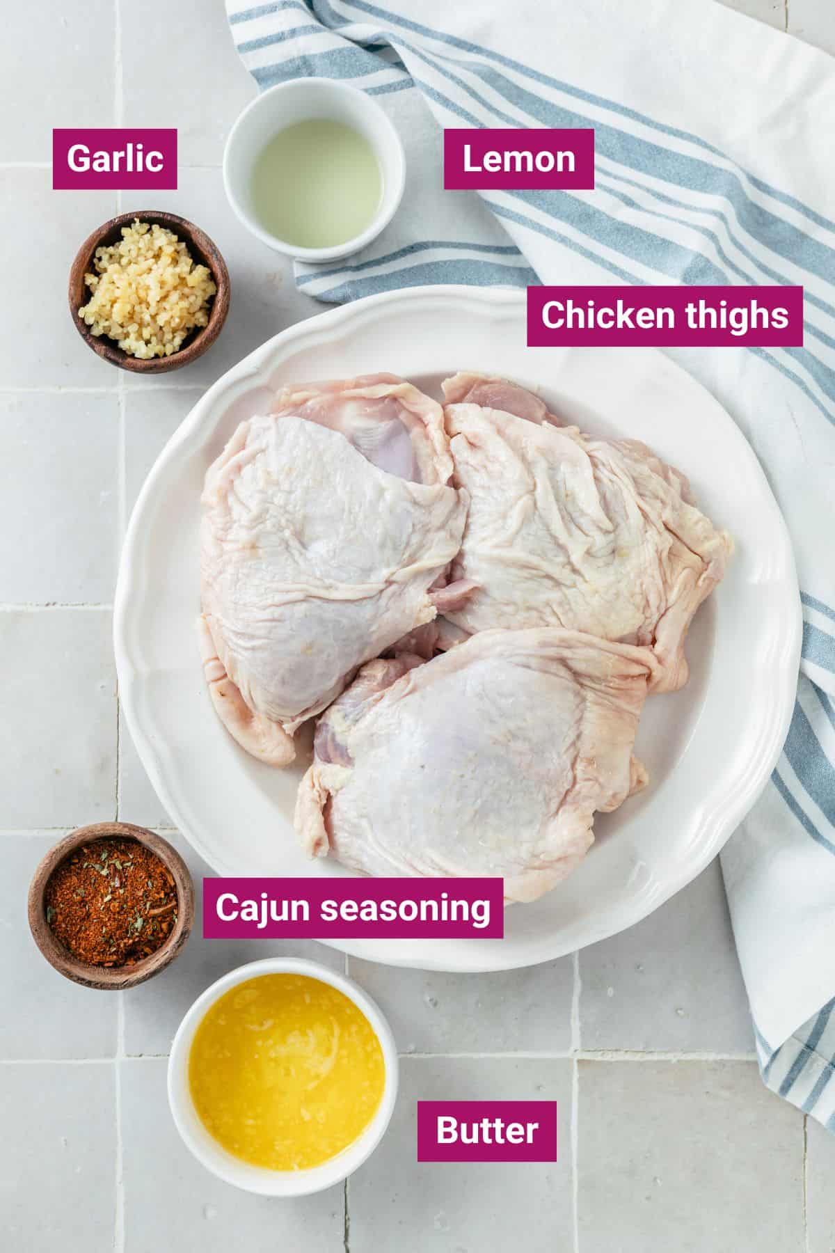 Ingredients for crispy baked bone-in chicken thighs beautifully arranged in separate bowls: chicken thighs (bone-in with skin), Cajun seasoning, melted salted butter, minced garlic, and lemon juice
