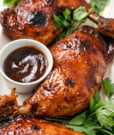 Crockpot BBQ Chicken Legs, glazed with rich barbecue sauce, served with a side of BBQ dip and garnished with fresh parsley.