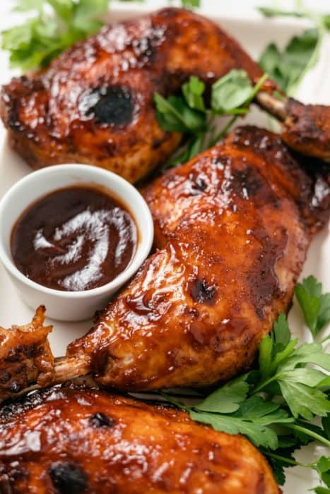 Crockpot BBQ Chicken Legs, glazed with rich barbecue sauce, served with a side of BBQ dip and garnished with fresh parsley.