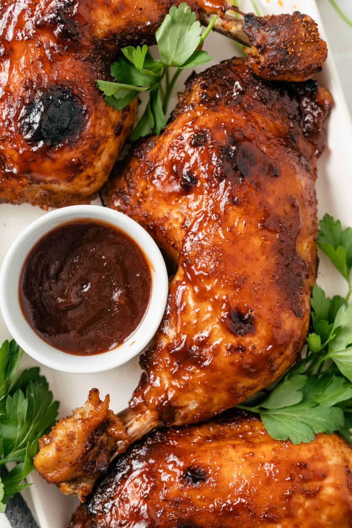 Succulent BBQ chicken quarters cooked in a slow cooker, coated in flavorful barbecue sauce, accompanied by a side of BBQ dip and garnished with fresh parsley.