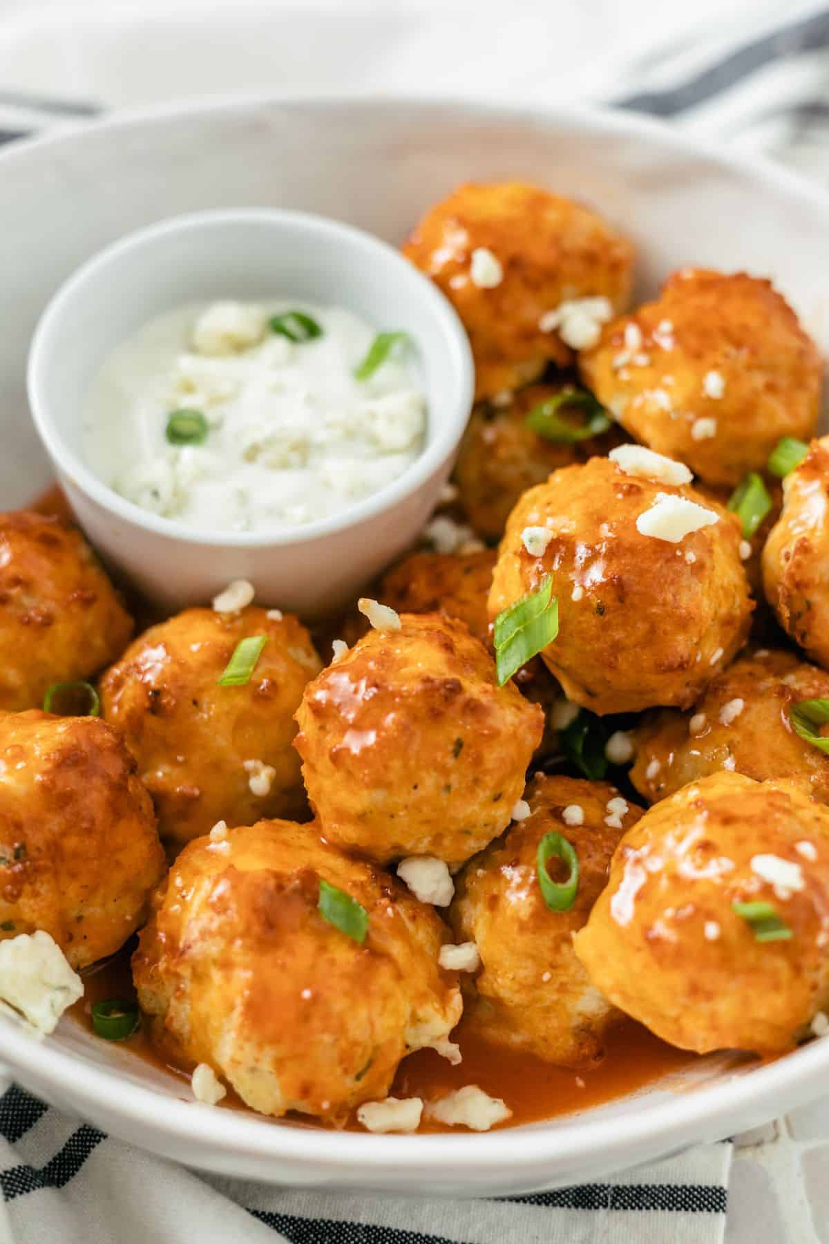 Bowl of Keto Buffalo Chicken Meatballs in a bowl with extra buffalo sauce, blue cheese crumbs, and green onions