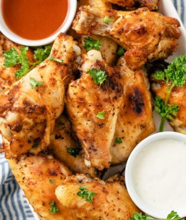 Slow Cooker Chicken Wings garnished with fresh parsley, accompanied by flavorful dips on the side