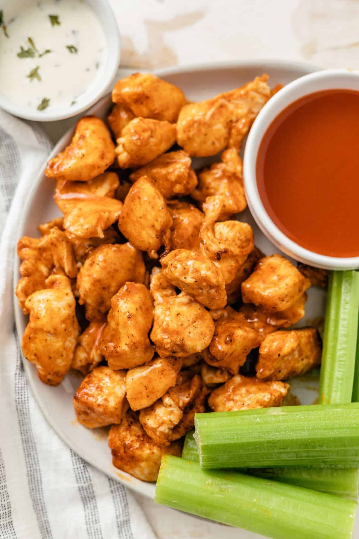 air fryer buffalo chicken bites with celery sticks, creamy blue cheese dressing and hot sauce on a plate