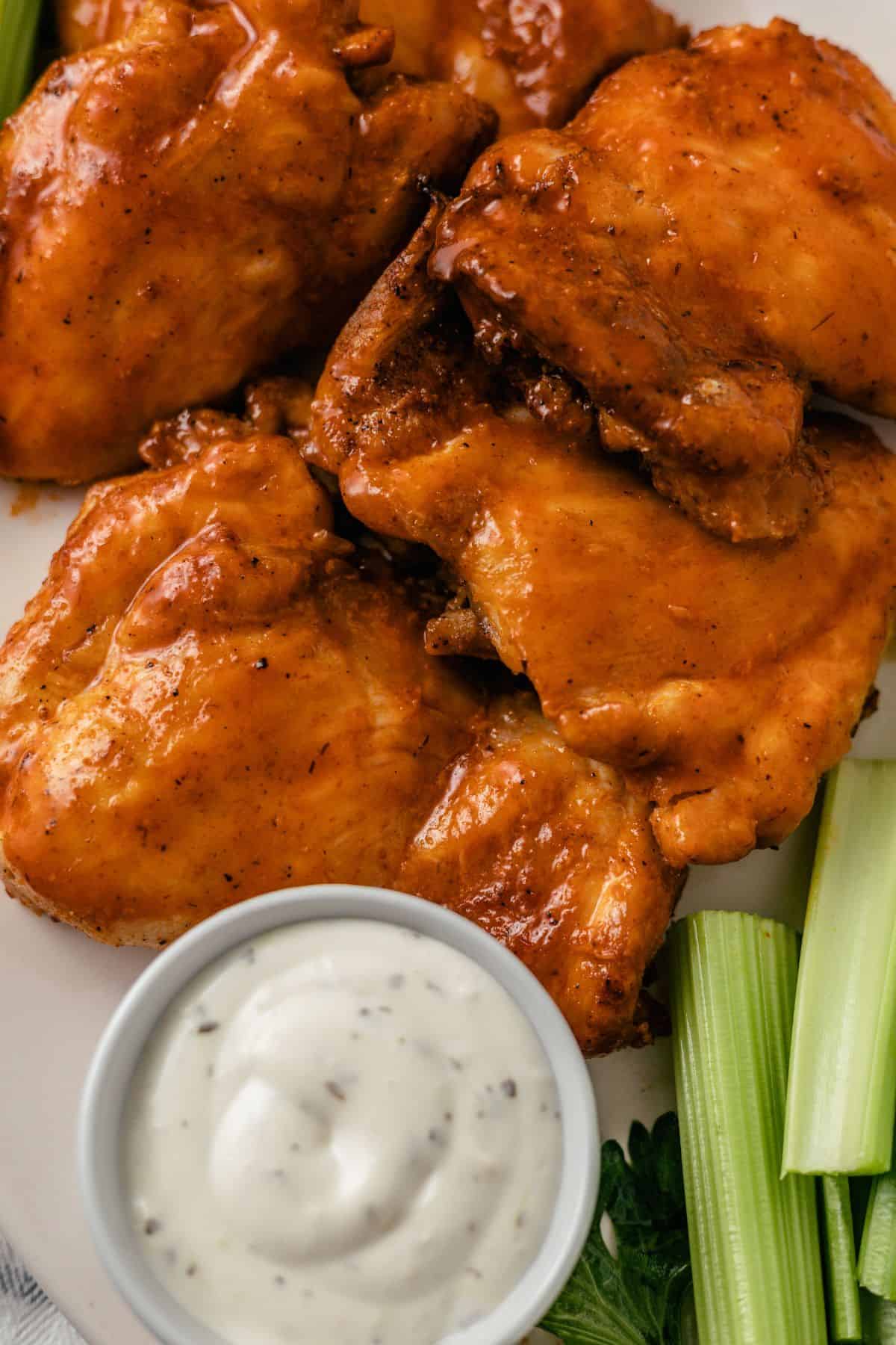 Five air fryer buffalo chicken thighs with creamy dipping sauce and celery sticks stacked on a plate