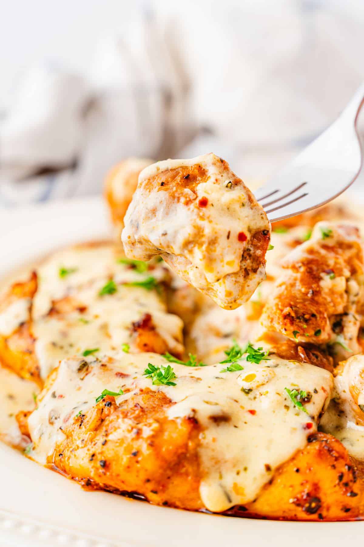 fork lifting a piece of creamy garlic parmesan chicken thighs