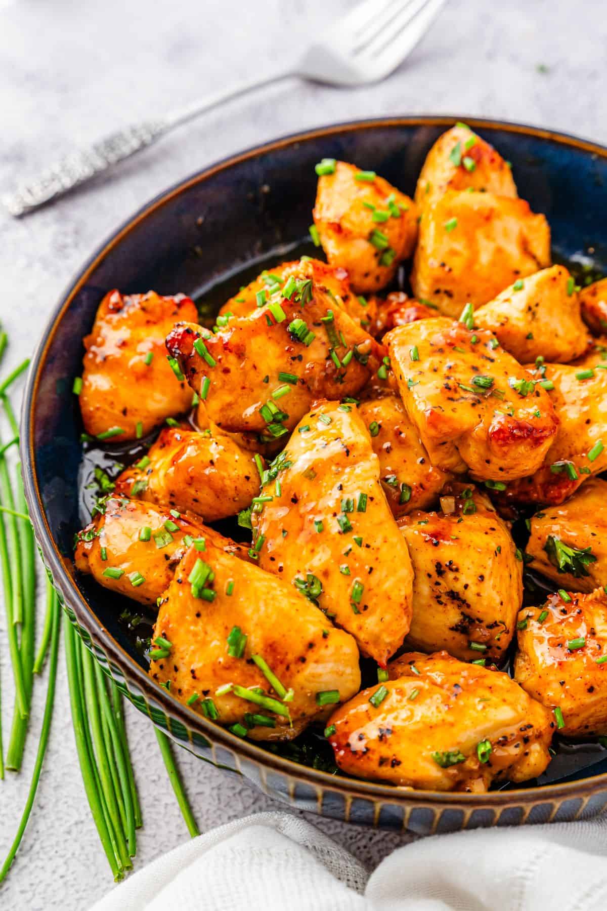 juicy honey garlic chicken bites topped with chives in a bowl