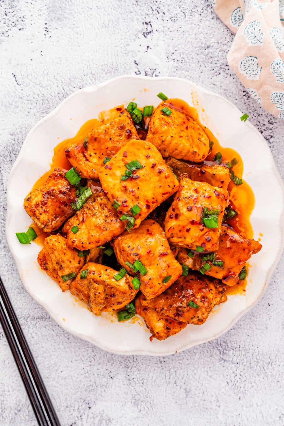 Juicy salmon bites coated in hot honey sauce, sprinkled with green onions